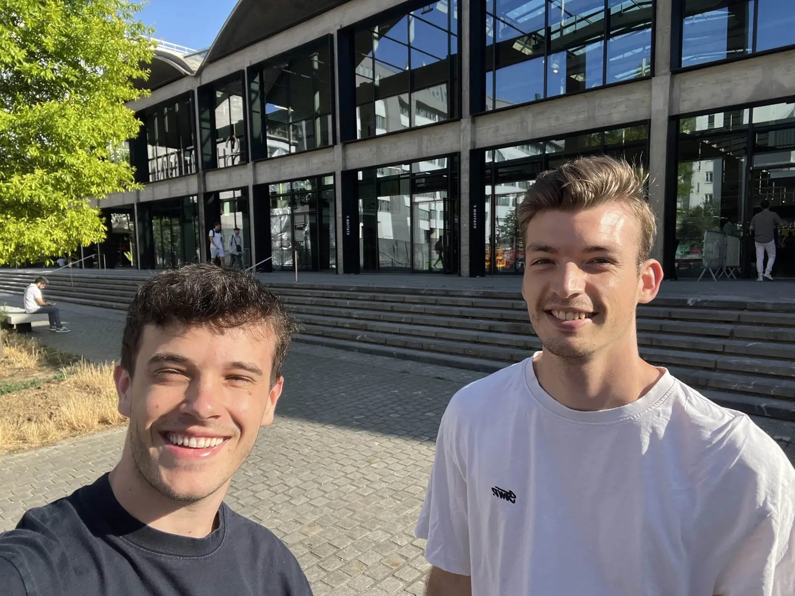 Two white young male taking a selfie in front of a building, they are smiling